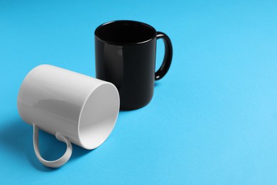 Photo of White and black ceramic mugs on light blue background, space for text