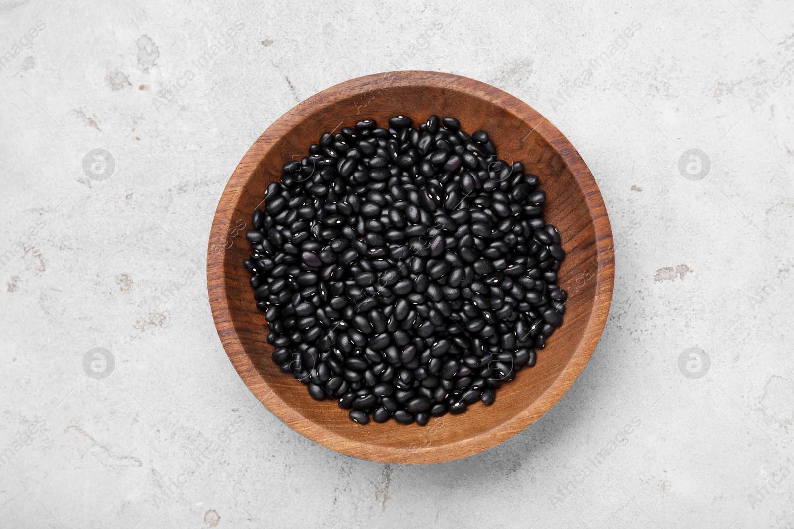 Photo of Bowl of raw black beans on light grey table, top view