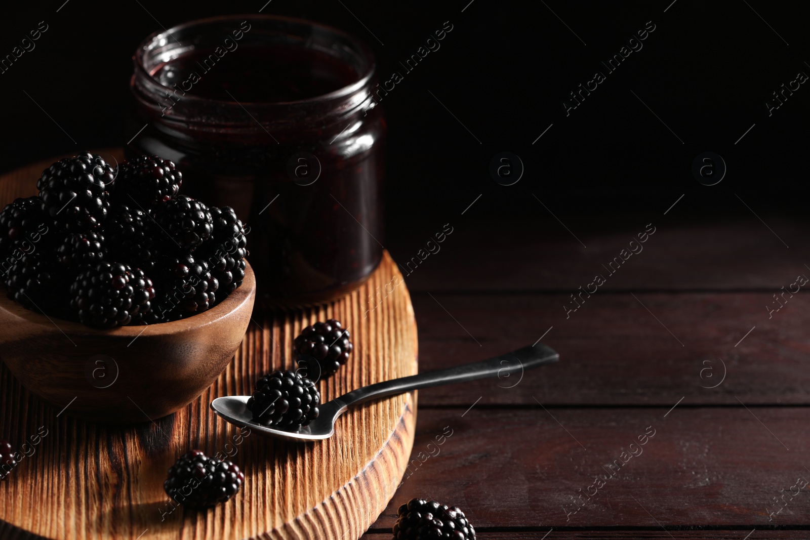 Photo of Fresh ripe blackberries and tasty jam on wooden table. Space for text