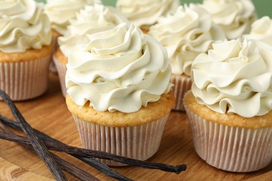 Photo of Tasty cupcakes with cream and vanilla pods on table, closeup