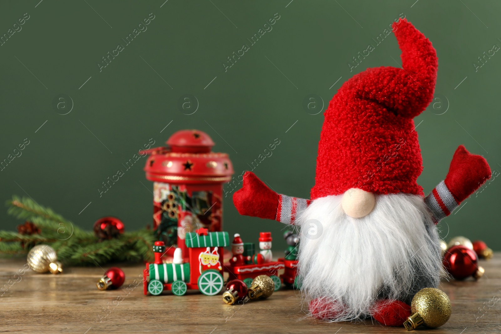 Photo of Cute Christmas gnome and festive decor on wooden table against green background. Space for text