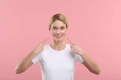 Photo of Woman showing her clean teeth and smiling on pink background