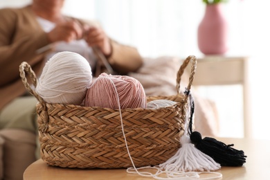 Photo of Basket with yarn and elderly woman knitting on background. Creative hobby