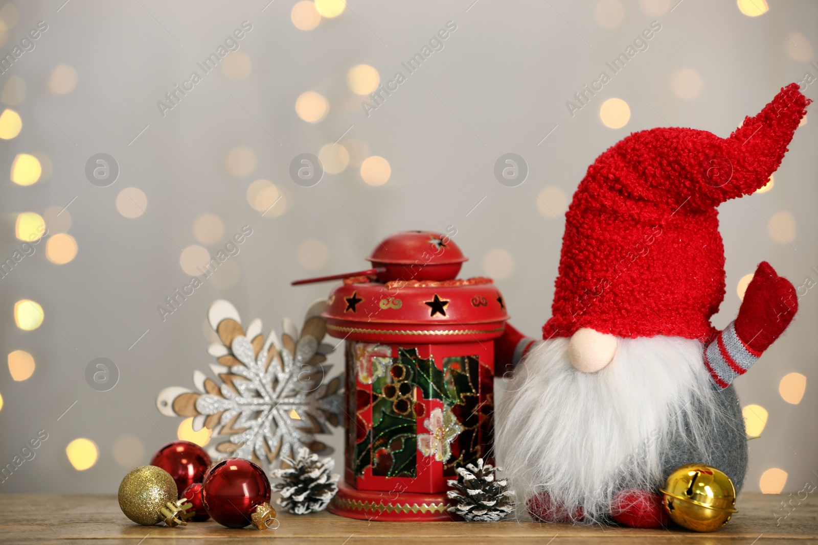 Photo of Cute Christmas gnome and festive decor on wooden table against blurred lights