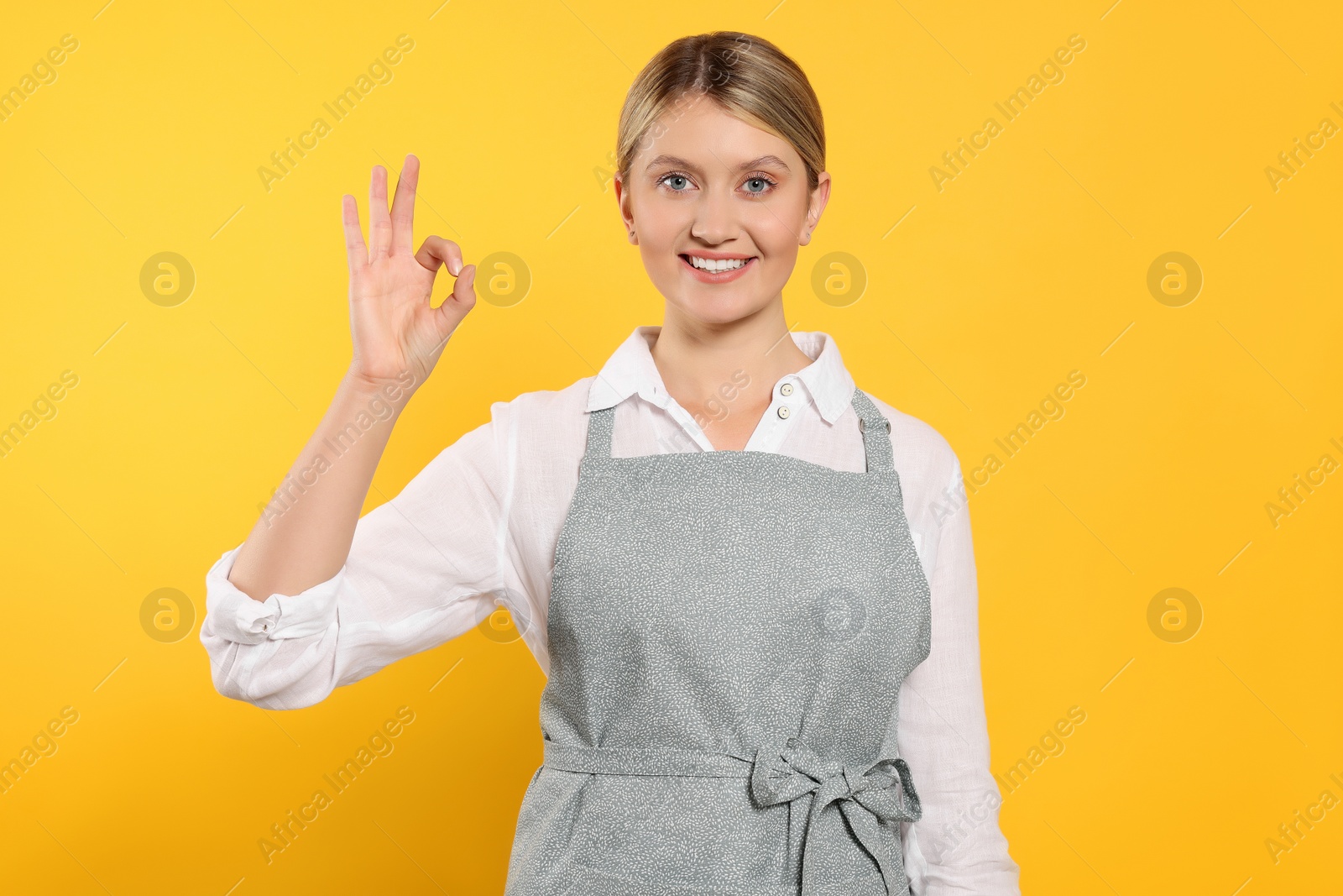 Photo of Beautiful young woman in clean apron with pattern on orange background