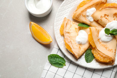 Photo of Delicious thin pancakes with oranges and cream on light table, flat lay