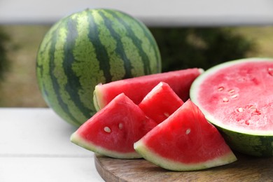 Photo of Delicious cut and whole ripe watermelons on white wooden table outdoors, closeup