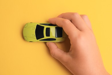 Photo of Child playing with toy car on yellow background, top view