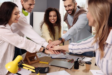 Photo of Team of employees putting hands together in office. Startup project