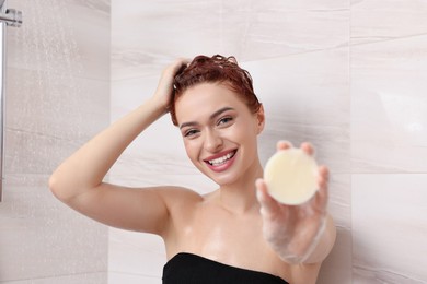Photo of Happy young woman with solid shampoo bar in shower