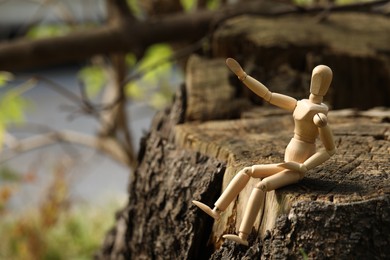 Photo of Wooden human figure sitting on stump outdoors, space for text