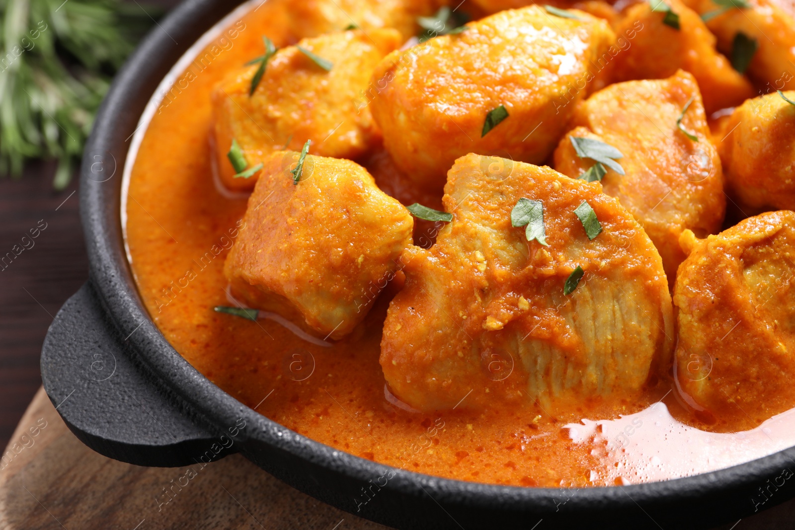 Photo of Delicious chicken curry in pan on wooden board, closeup