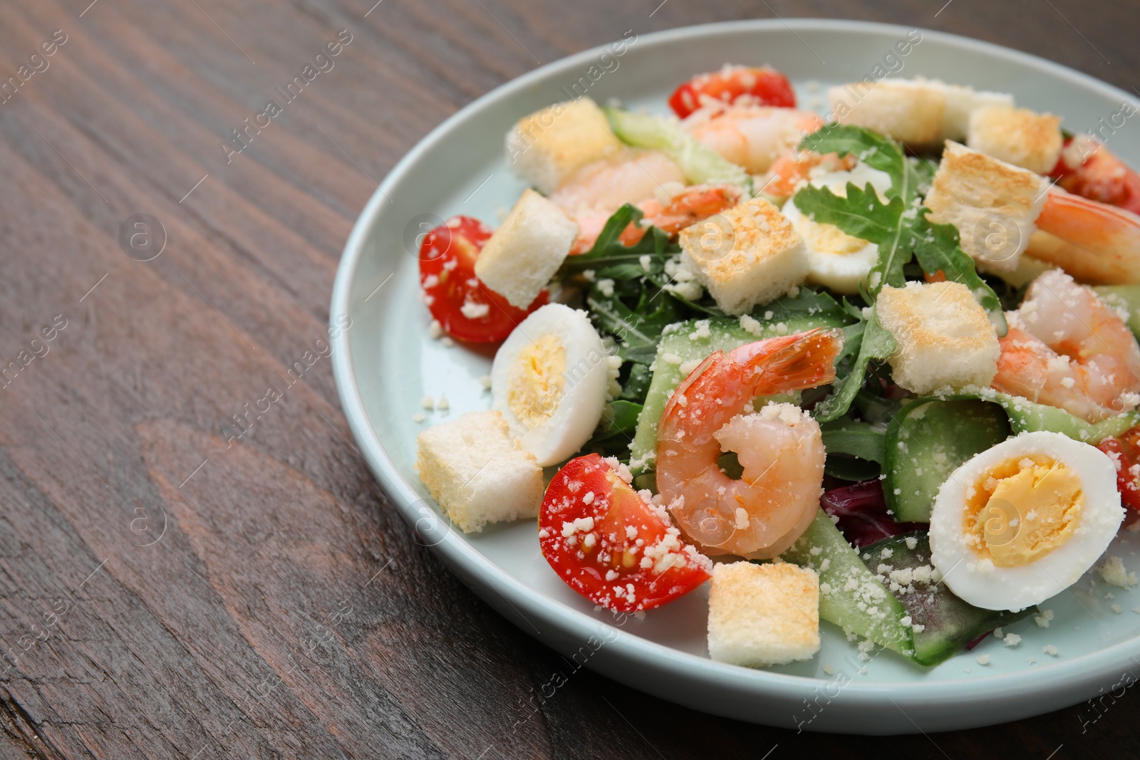 Photo of Delicious Caesar salad with shrimps on wooden table, closeup. Space for text