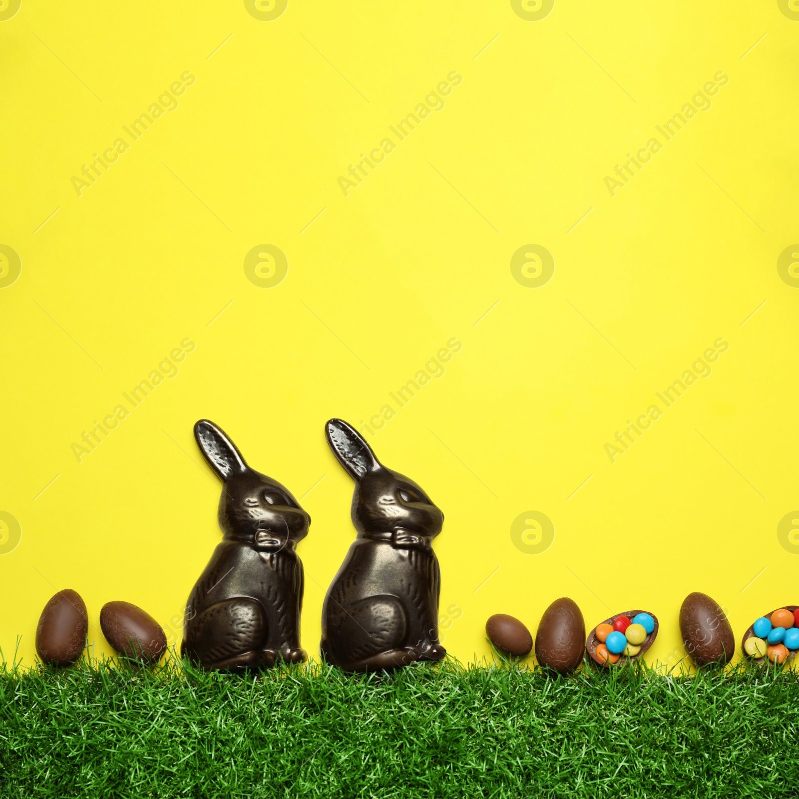 Photo of Chocolate Easter bunnies, egg and candies with green grass on yellow background