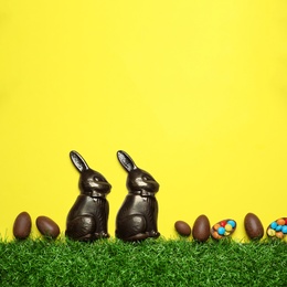 Photo of Chocolate Easter bunnies, egg and candies with green grass on yellow background