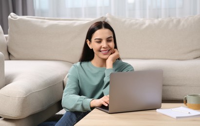 Photo of Happy woman working with laptop at coffee table in living room