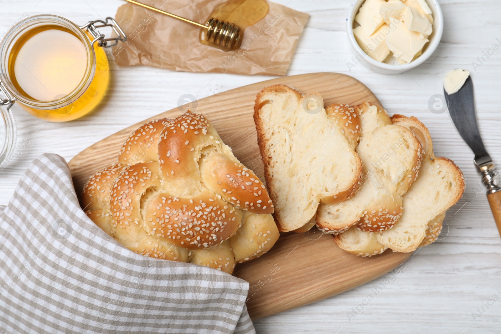 Photo of Cut freshly baked braided bread, honey and butter on white wooden table, flat lay. Traditional Shabbat challah