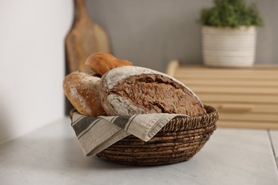 Photo of Wicker bread basket with freshly baked loaves on white marble table in kitchen