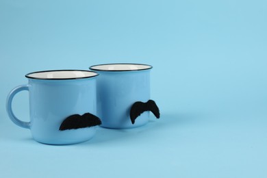 Photo of Cups with fake mustaches on light blue background. Space for text