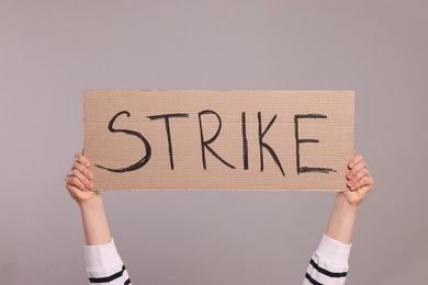 Photo of Woman holding cardboard banner with word Strike on light grey background, closeup