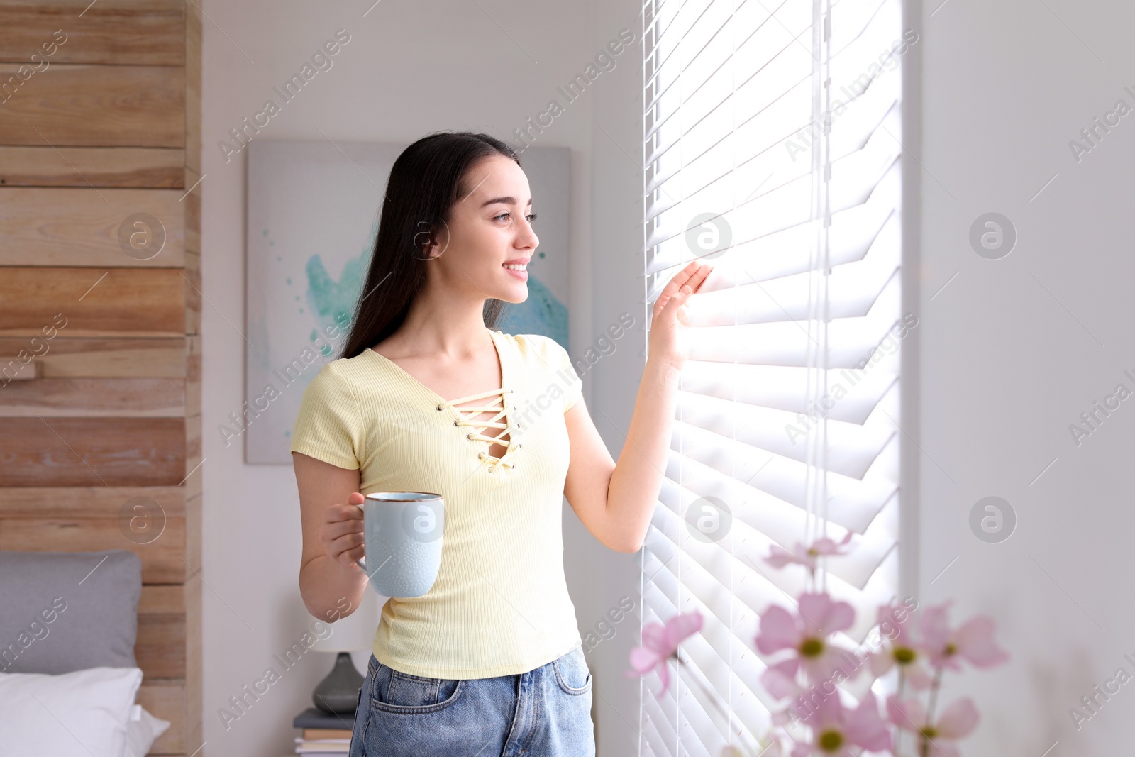Photo of Young woman with cup of hot drink near window in modern bedroom. Elegant interior