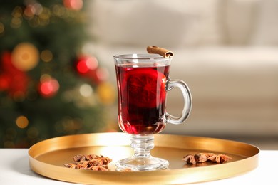 Delicious mulled wine in glass cup and anise stars on white table against blurred background