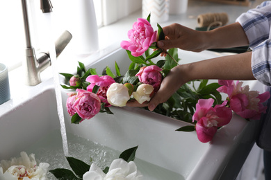 Woman with beautiful peonies near kitchen sink, closeup