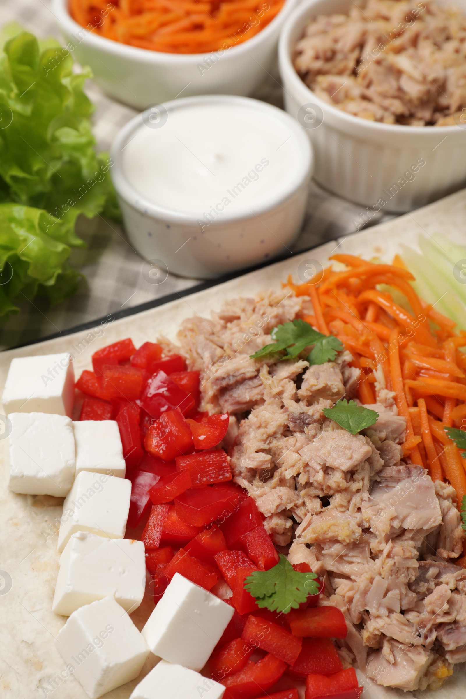 Photo of Delicious tortilla with tuna and vegetables on table, closeup. Cooking shawarma