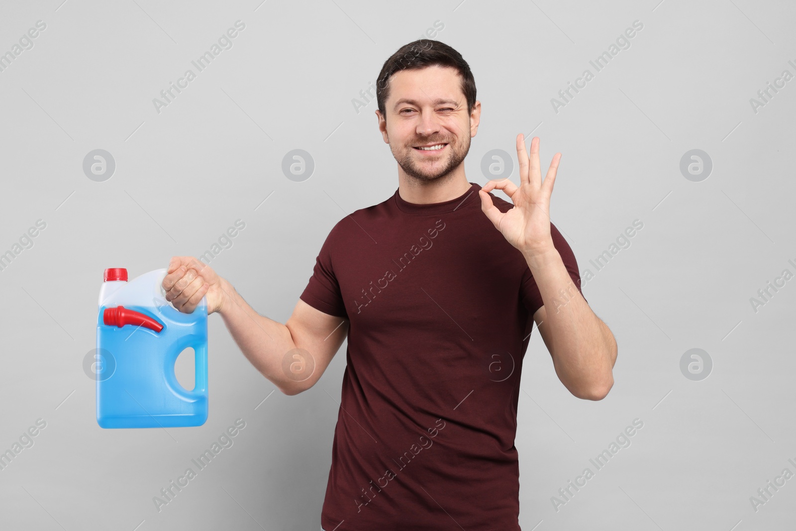 Photo of Man holding canister with blue liquid and showing OK gesture on light grey background