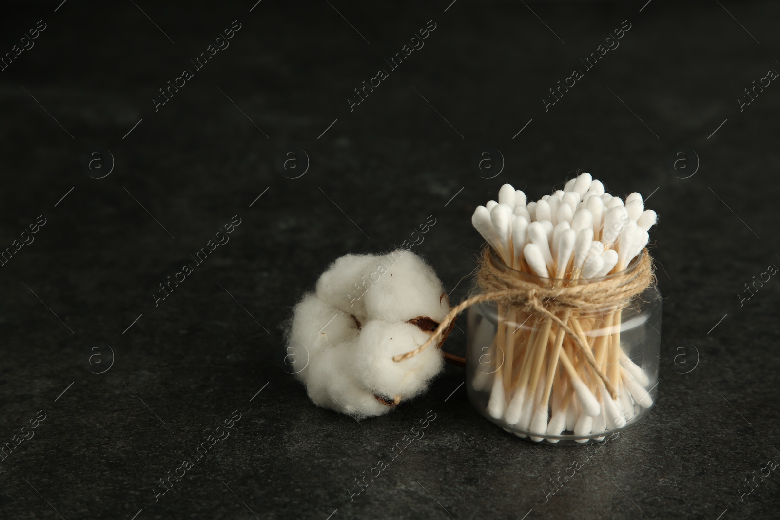 Photo of Cotton swabs and flower on black table, space for text