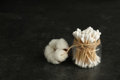 Photo of Cotton swabs and flower on black table, space for text