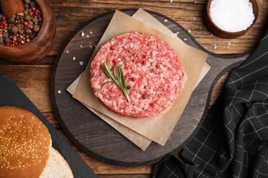 Photo of Raw hamburger patties with rosemary and spices on wooden table, flat lay