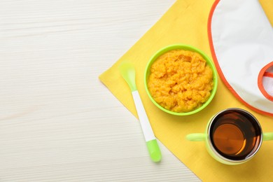 Photo of Baby bib and plastic dishware with healthy food on white wooden table, flat lay. Space for text