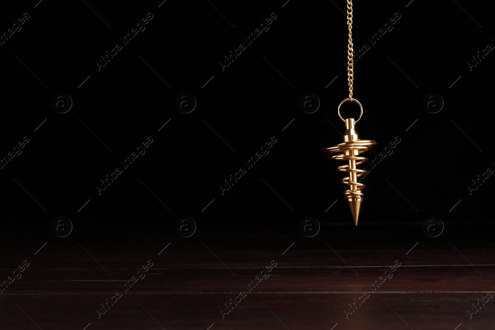 Photo of Stylish pendulum above wooden table on black background, space for text. Hypnotherapy session