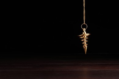 Stylish pendulum above wooden table on black background, space for text. Hypnotherapy session