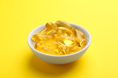 Photo of Vitamin capsules in bowl on yellow background