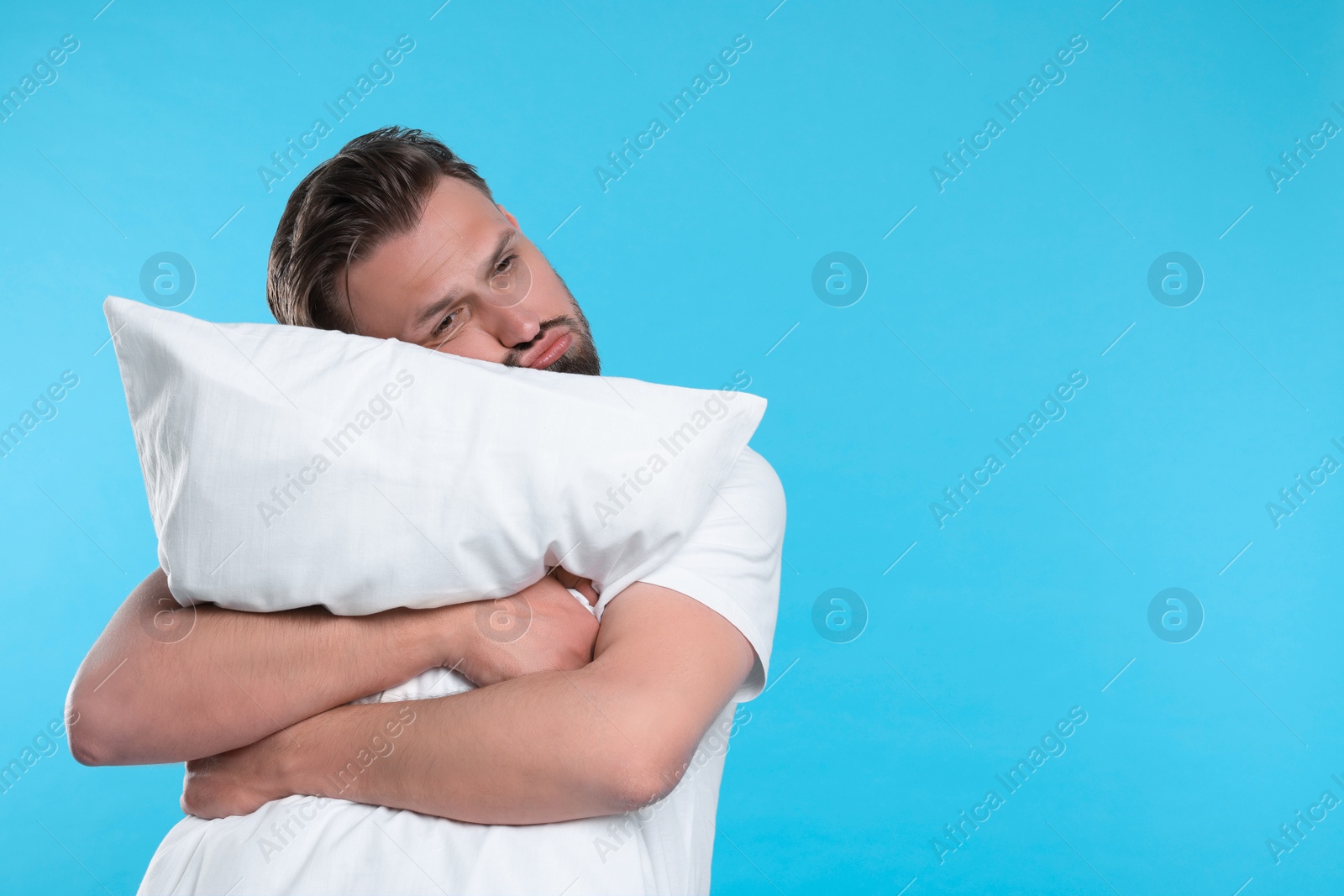 Photo of Unhappy man with pillow on light blue background, space for text. Insomnia problem