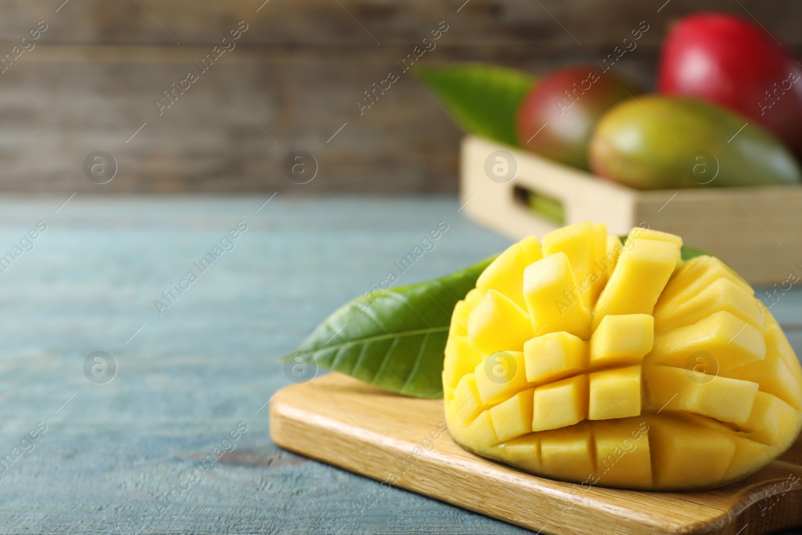 Photo of Cut fresh ripe mango on blue wooden table. Space for text