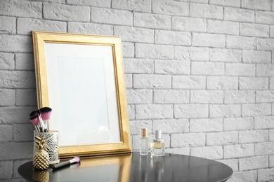 Photo of Mockup of blank frame and makeup brushes on table