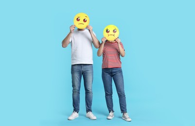 People covering faces with emoticons on light blue background