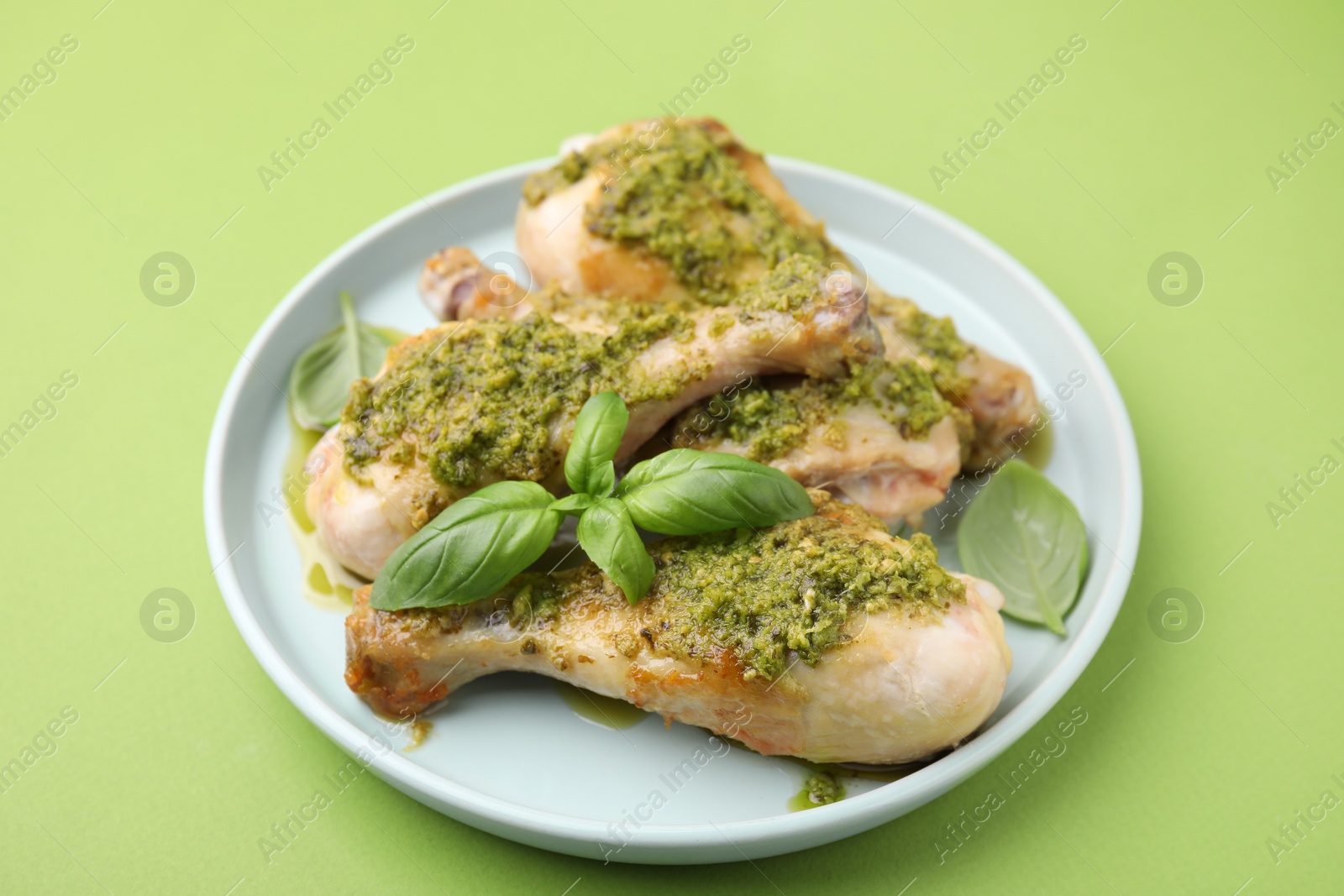 Photo of Delicious fried chicken drumsticks with pesto sauce and basil on green table