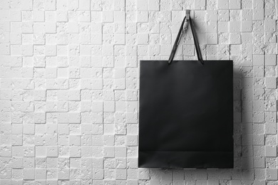Photo of Paper shopping bag with ribbon handles hanging on white wall. Mockup for design