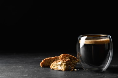 Photo of Tasty cantucci and cup of aromatic coffee on black table, space for text. Traditional Italian almond biscuits