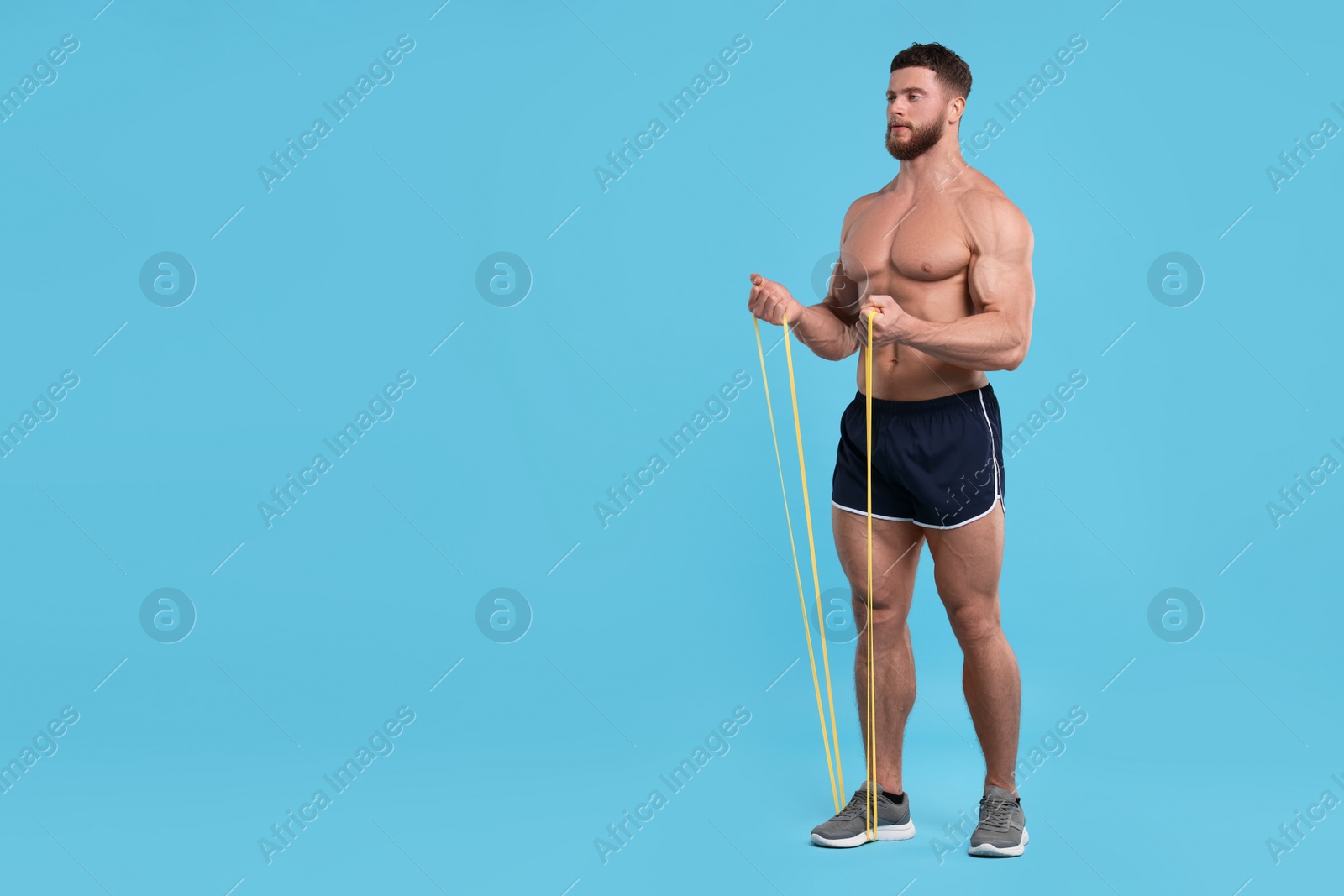 Photo of Young man exercising with elastic resistance band on light blue background. Space for text