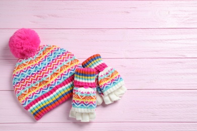 Warm knitted hat and mittens on pink wooden background, flat lay. Space for text
