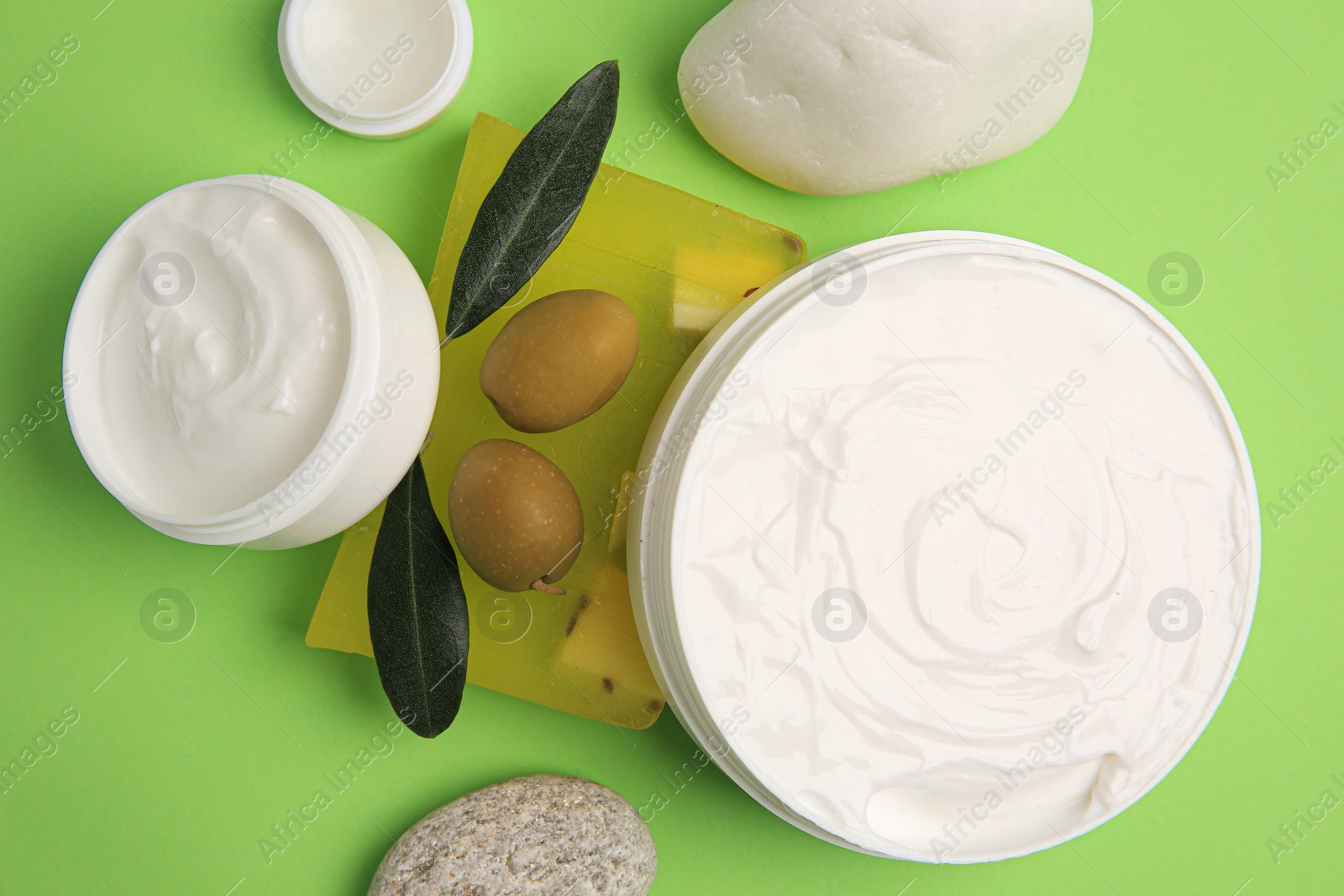 Photo of Different cosmetic products with olives and stones on light green background, flat lay