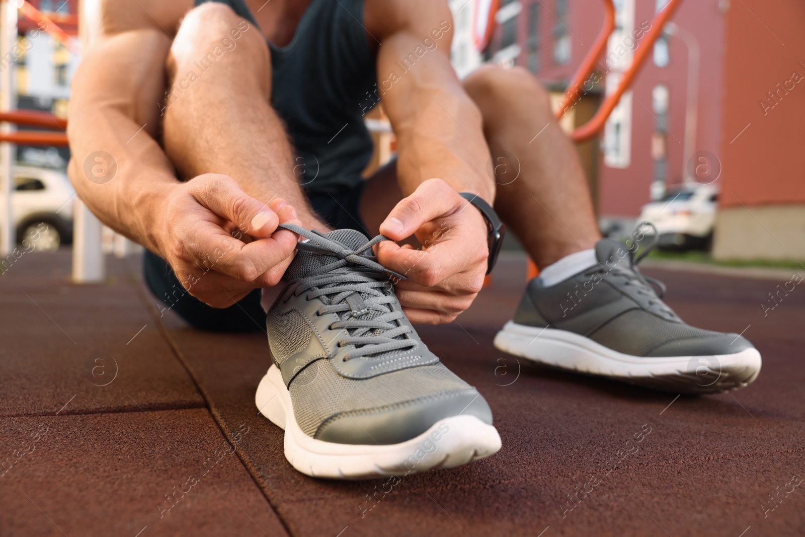 Photo of Man tying shoelaces before training at outdoor gym, closeup