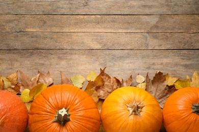 Photo of Flat lay composition with pumpkins and autumn leaves on wooden table. Space for text