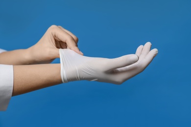 Photo of Doctor putting on medical gloves against blue background, closeup
