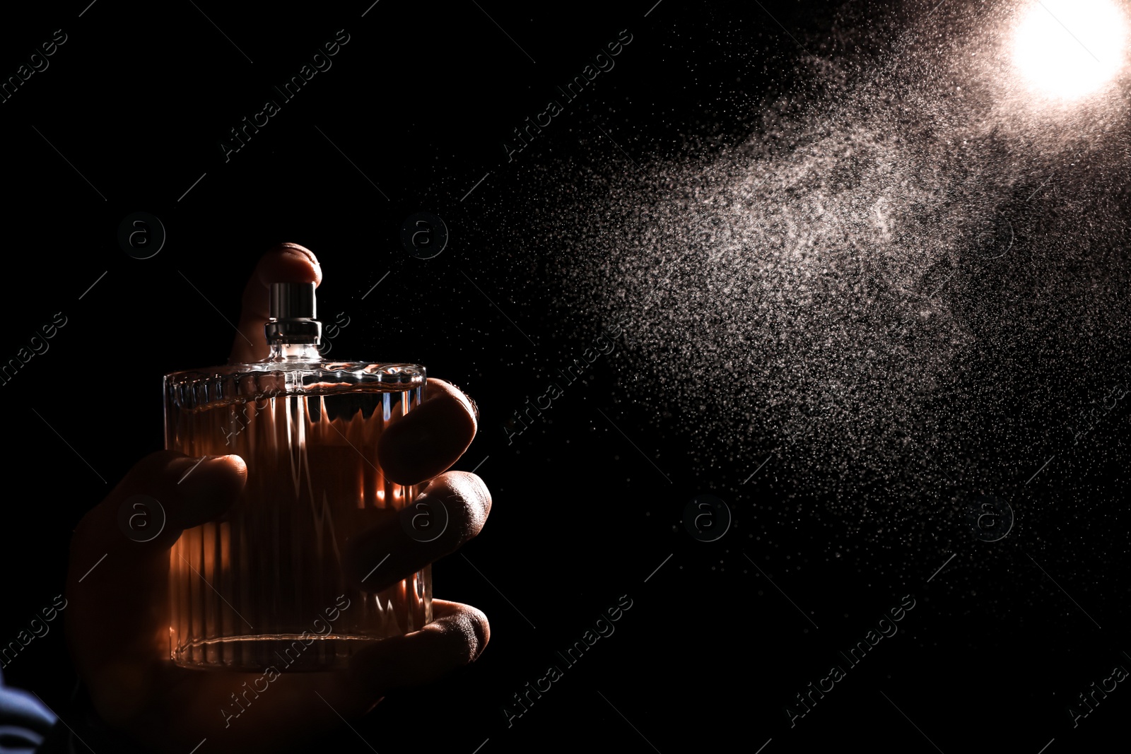 Photo of Man spraying luxury perfume on black background, closeup